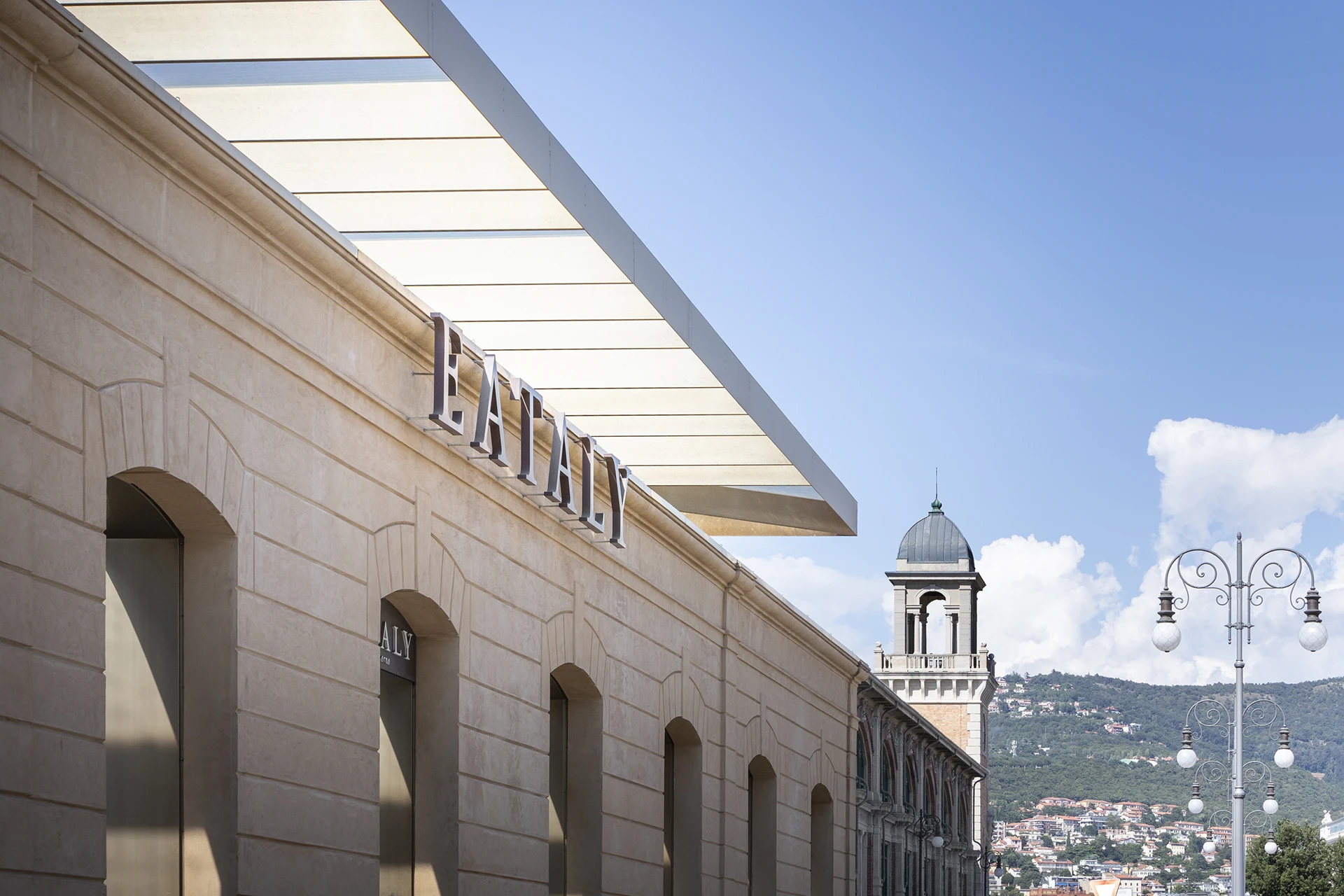 Eataly Trieste e Salone degli Incanti sul waterfront cittadino, con architettura storica, portici e vista sulle colline del Carso sullo sfondo