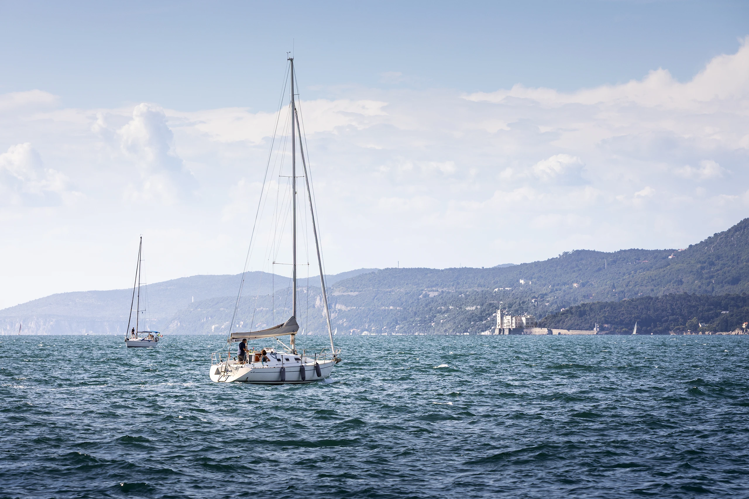 Vista dal Molo Audace verso il Castello di Miramare a Trieste, con barche a vela in primo piano e costa affacciata sul Golfo